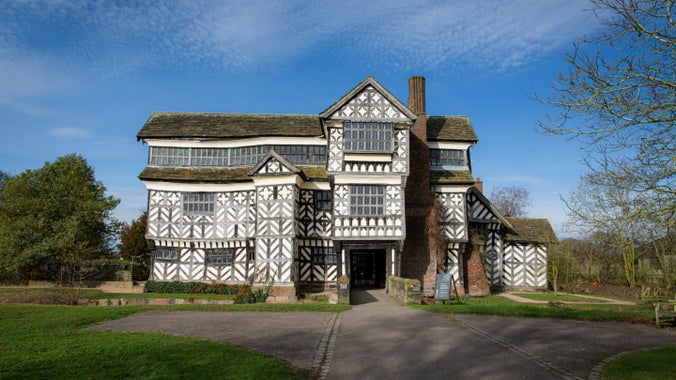 Exterior of the iconic wood frame moated Tudor manor house with black and white features and a blue sky in the background